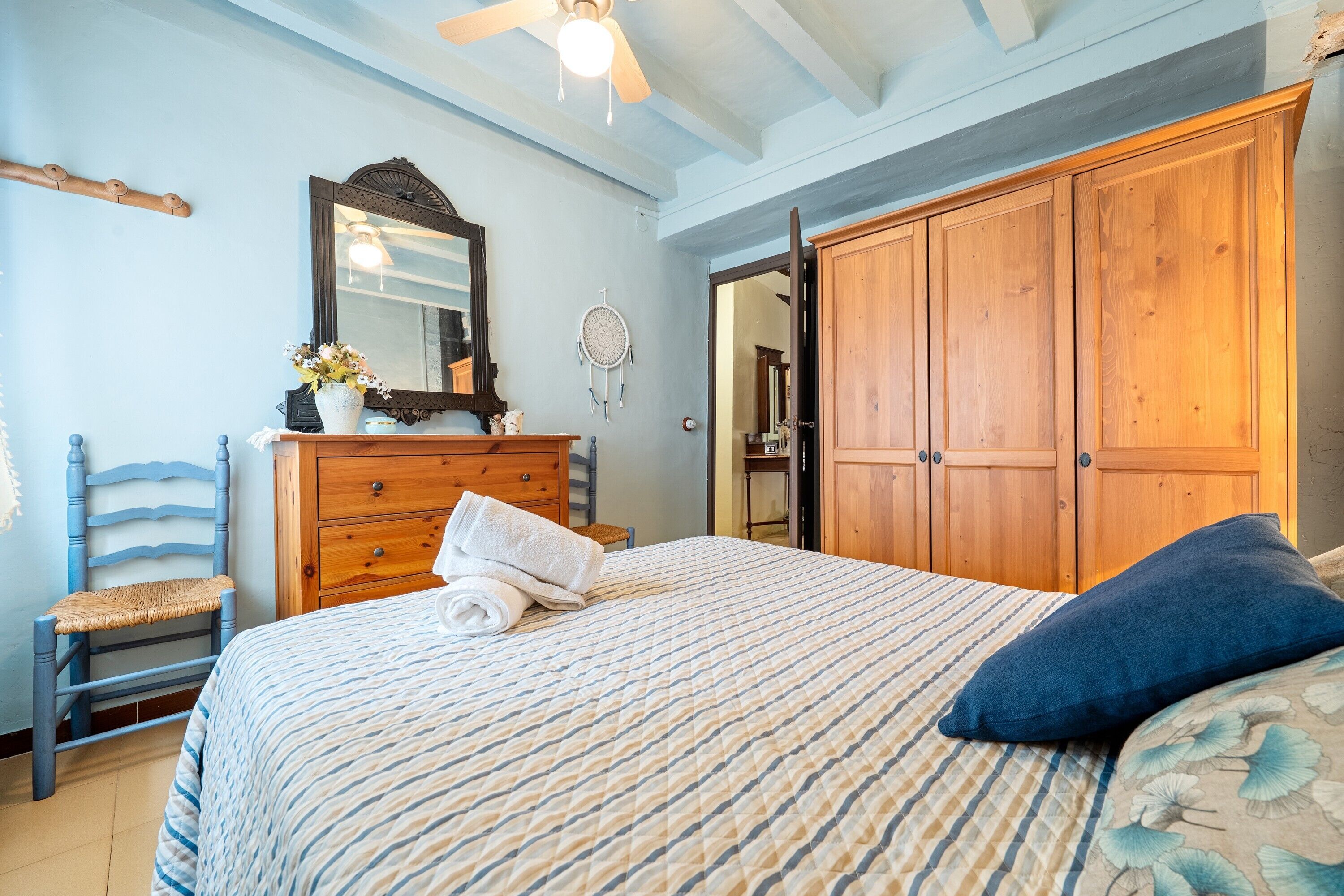 Una camera da letto con un letto, un armadio in legno, una cassettiera, una sedia e una ventola a soffitto.