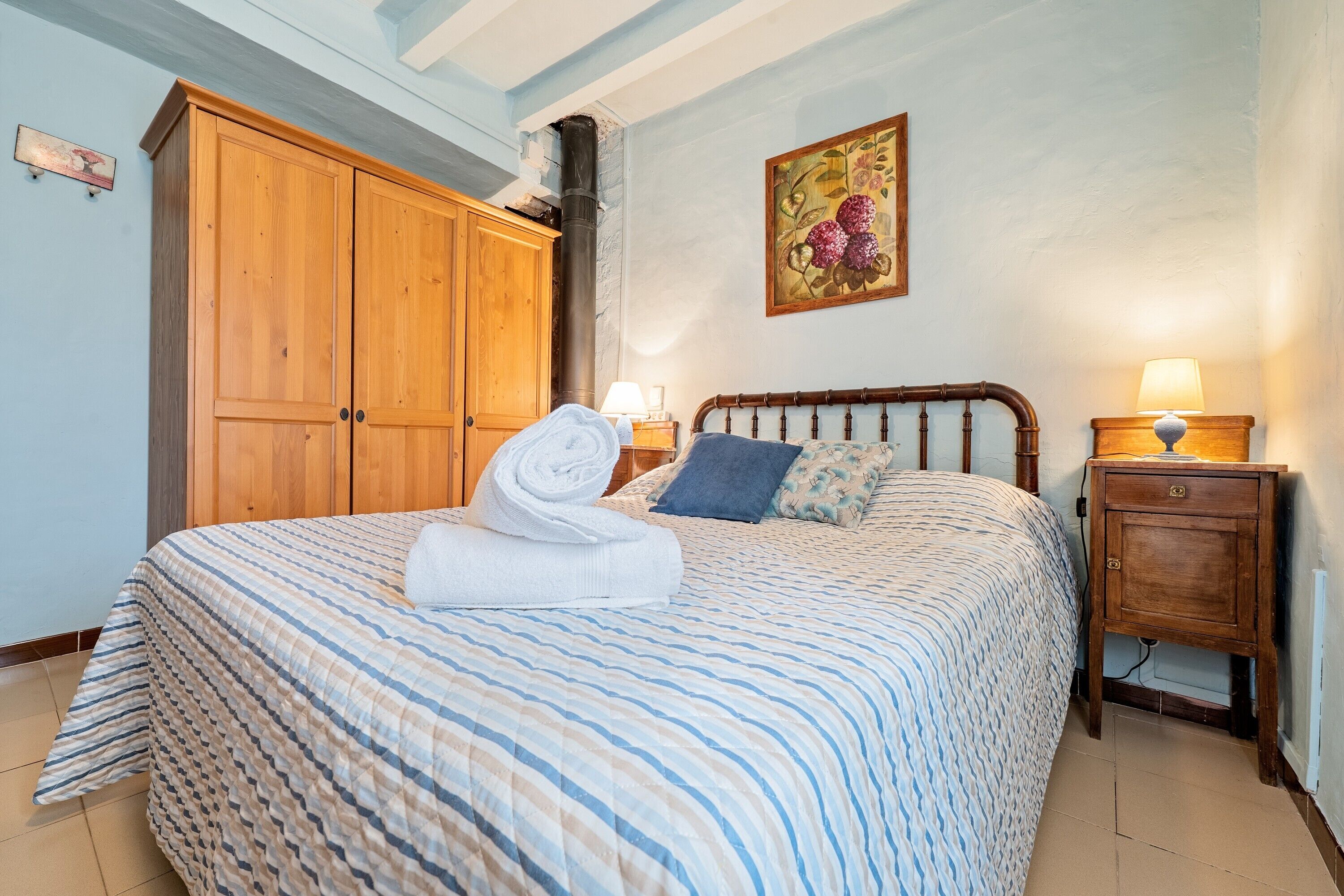 Un dormitorio con cama, armario de madera y mesita de noche con lámpara.