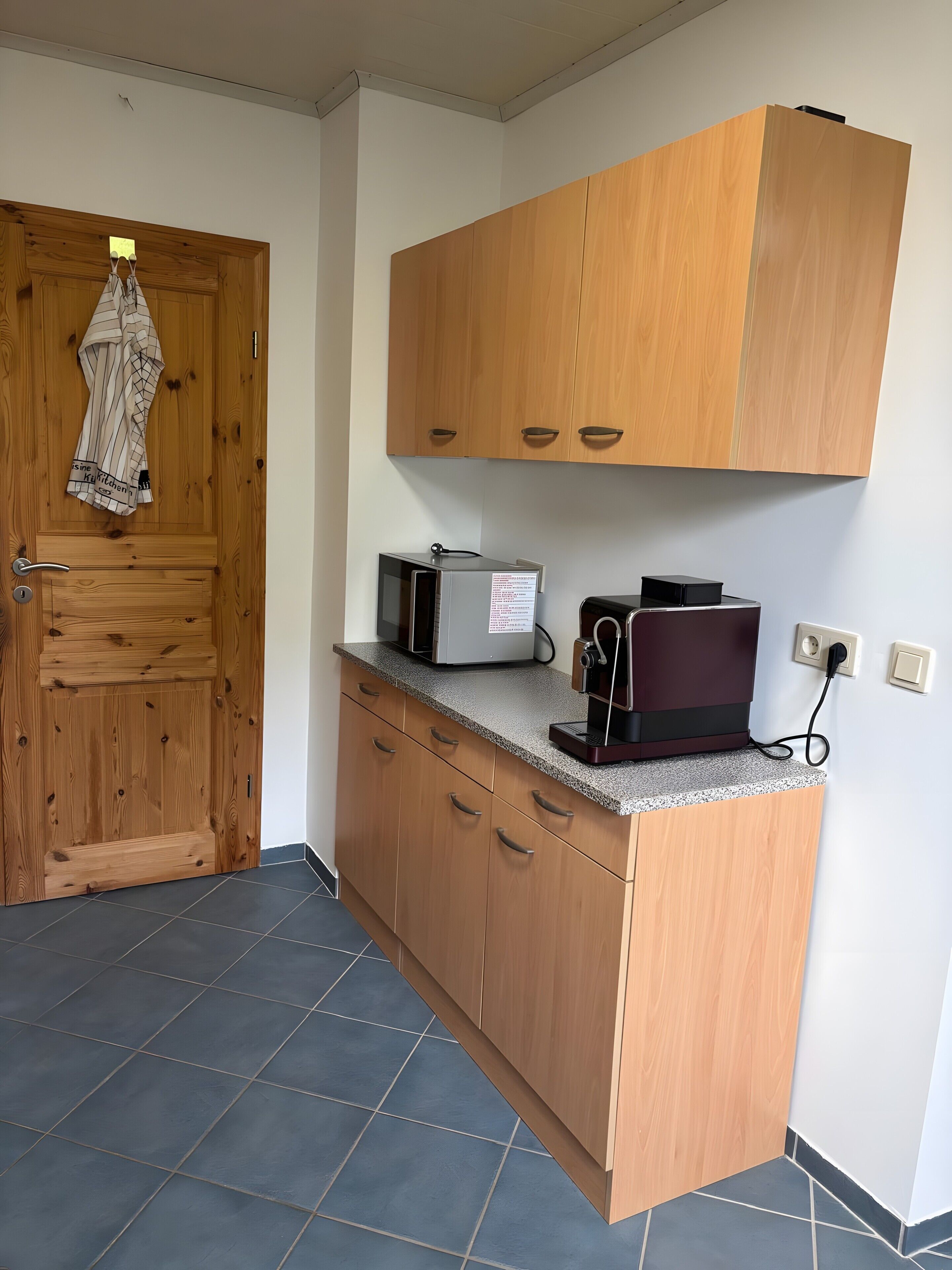 A kitchen with wooden cabinets, a microwave, a coffee maker, and a door with a towel hanging.