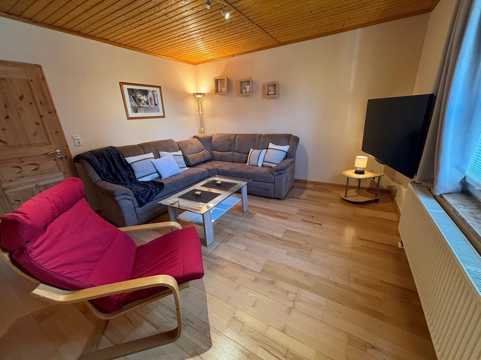 A living room with a sectional sofa, a red armchair, a coffee table, a TV, and a lamp.