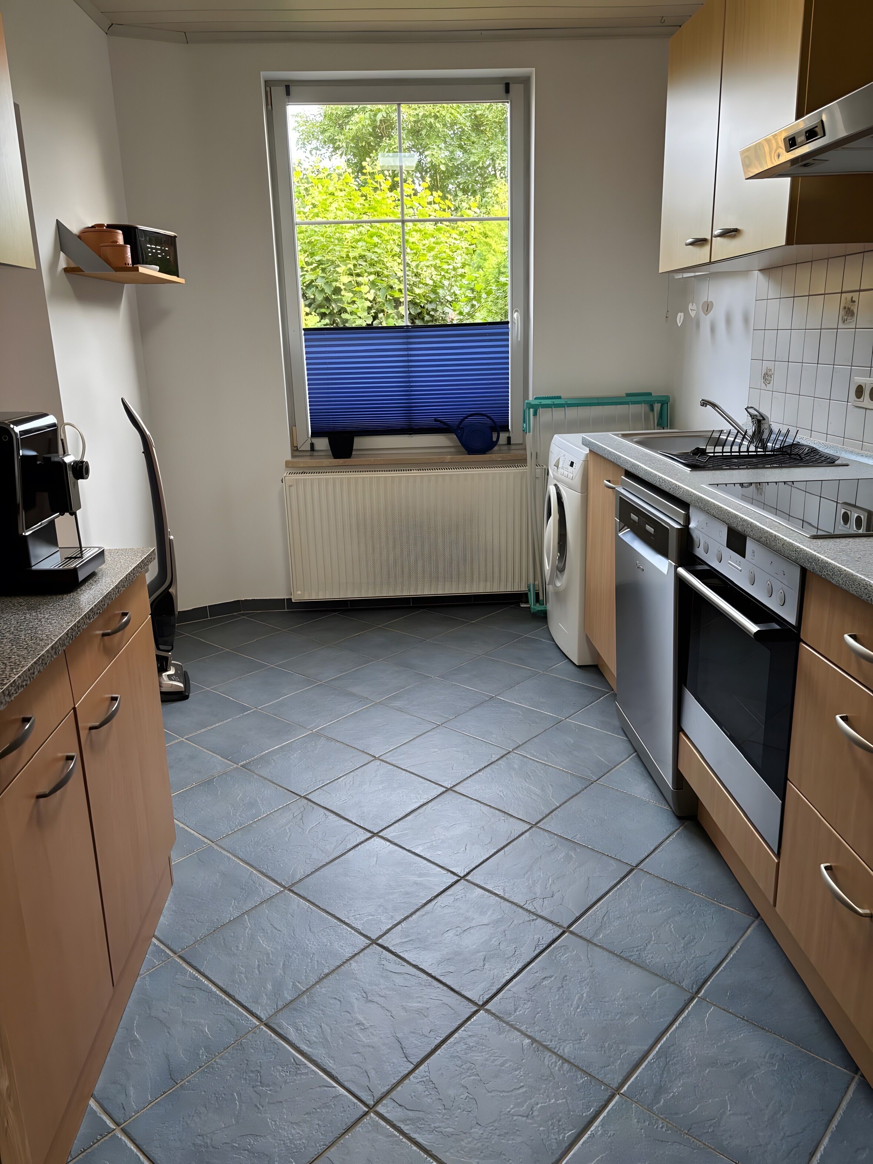 A kitchen with a built-in washing machine, a coffee maker, and a window with a view of greenery.