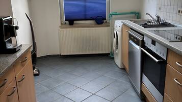 A kitchen with a built-in washing machine, a coffee maker, and a window with a view of greenery.