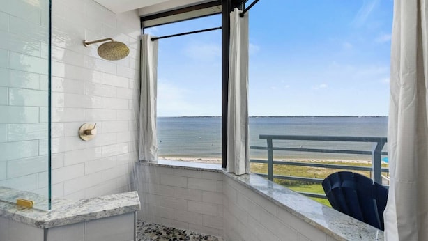 Casa de banho com chuveiro, porta de vidro e vista para o mar.
