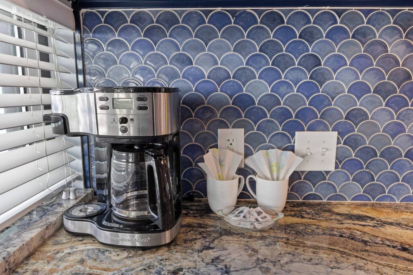 A coffee maker on a granite countertop with a blue tiled backsplash.