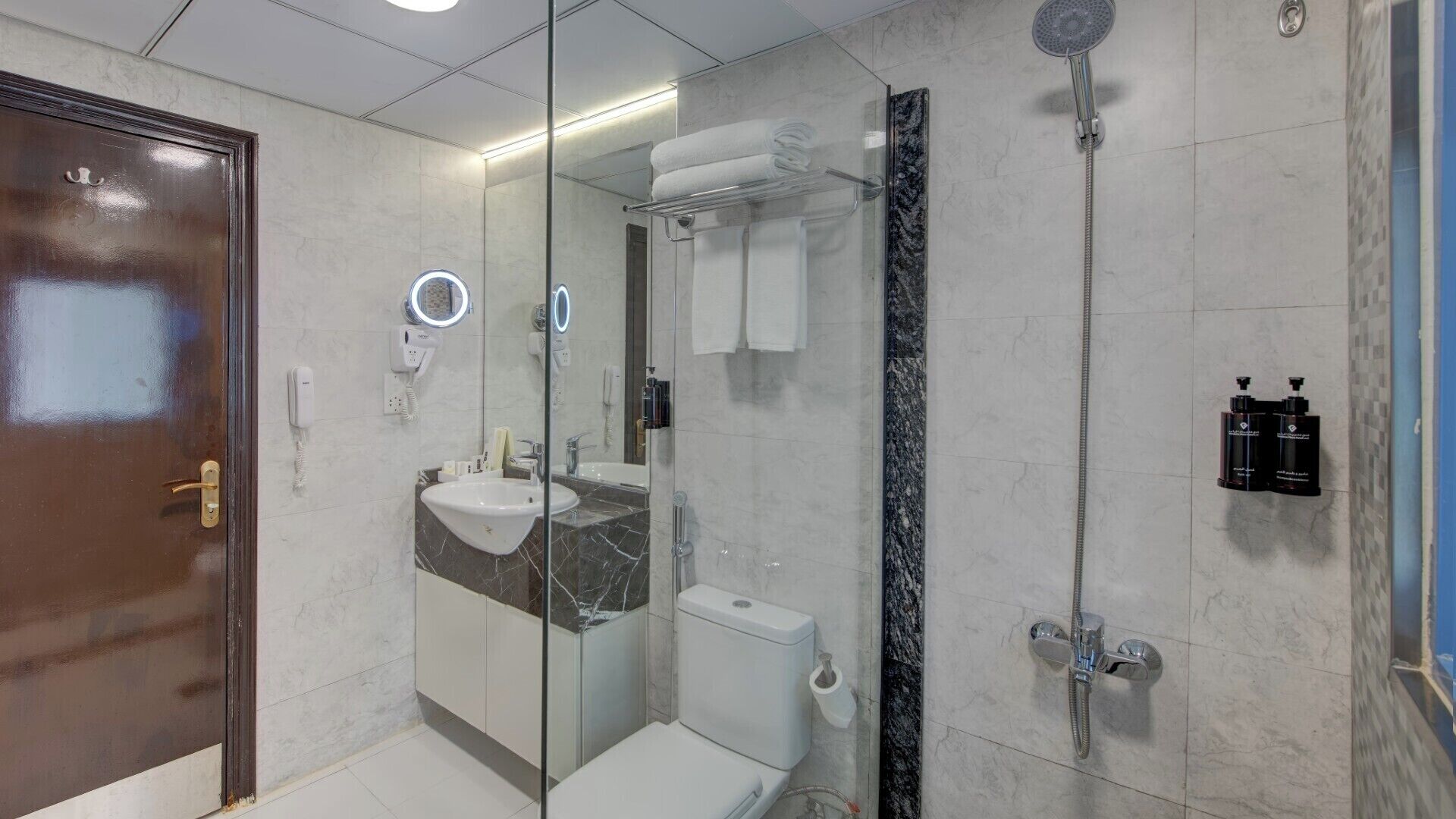 Un baño moderno con cabina de ducha de vidrio, lavamanos con encimera de mármol y inodoro.