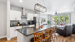 A modern kitchen with white cabinets, a central island with bar stools, a microwave, and a stove.