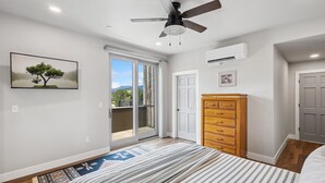 A bedroom with a bed, a ceiling fan, a wardrobe, a door, and a window with a view.