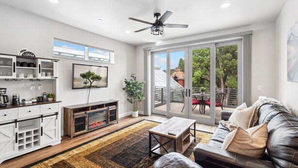 A modern living room with a leather sofa, a coffee table, and a fireplace. There is a sliding glass door leading to an outdoor patio with a table and chairs.
