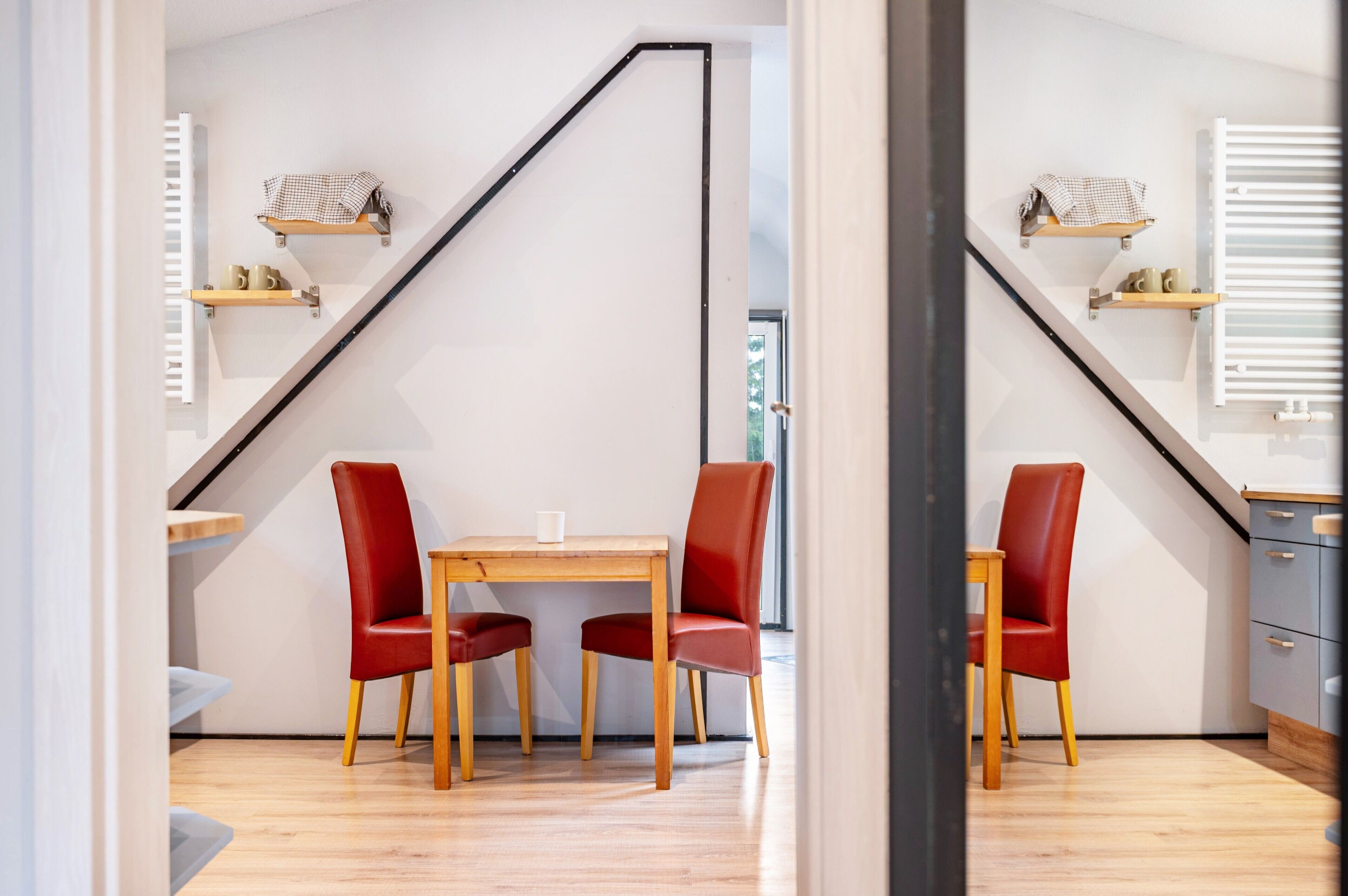 A dining area with a table and chairs, a staircase, and shelves with items.