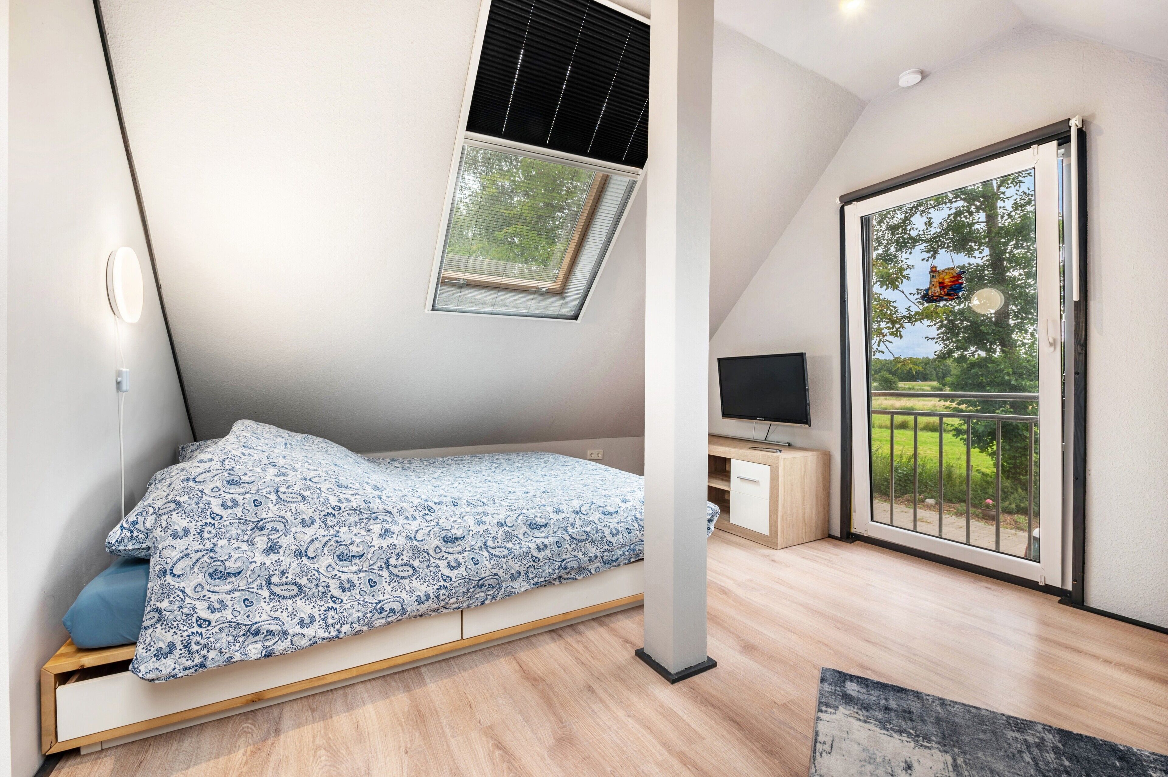 A bedroom with a skylight, a bed, a TV, and a sliding glass door to the outside.