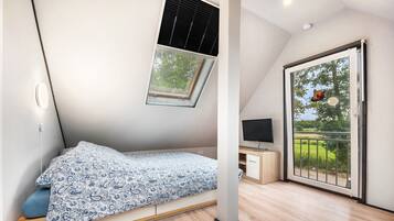 A bedroom with a skylight, a bed, a TV, and a sliding glass door to the outside.