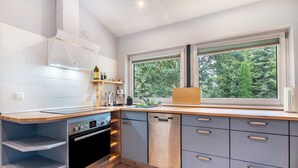 A modern kitchen with a built-in oven, dishwasher, and a window with a view of trees. - Apartment 'Kanal' with Private Terrace and Wi-Fi (Steinau)