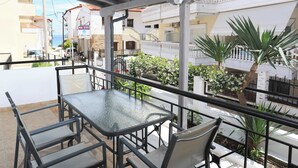 A balcony with a glass table and chairs, surrounded by railings and plants. - Gregory Apartments  (Kassandra)