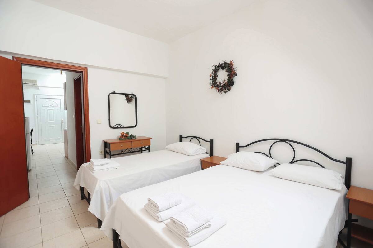 Habitación de hotel con dos camas, una mesita de noche de madera, un aparador, un espejo y una corona decorativa en la pared.