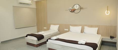 A hotel room with two beds, a ceiling fan, an air conditioner, a clock, and a bedside table with a phone.