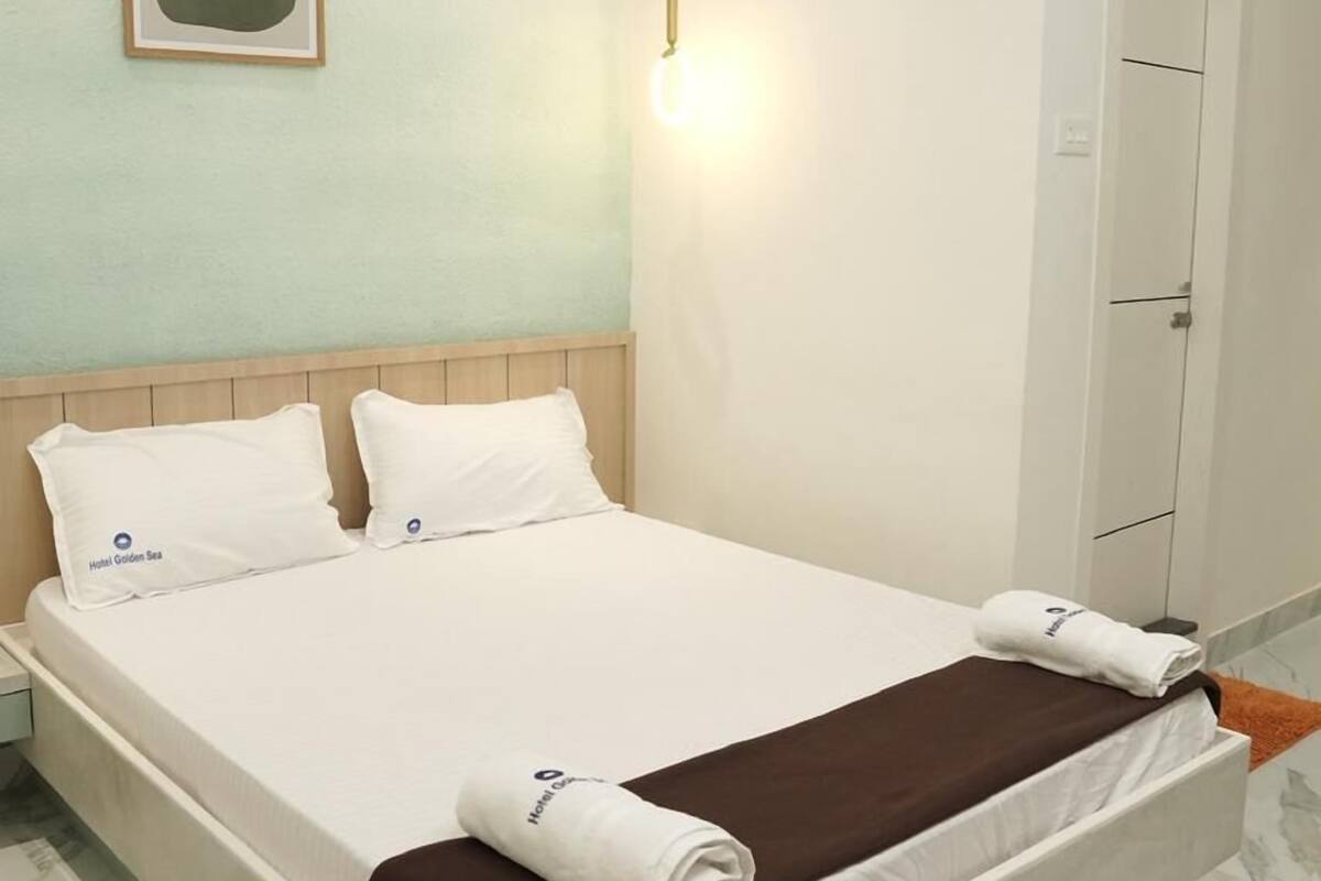 A hotel room with a bed, a nightstand, a wall-mounted light, and a door.