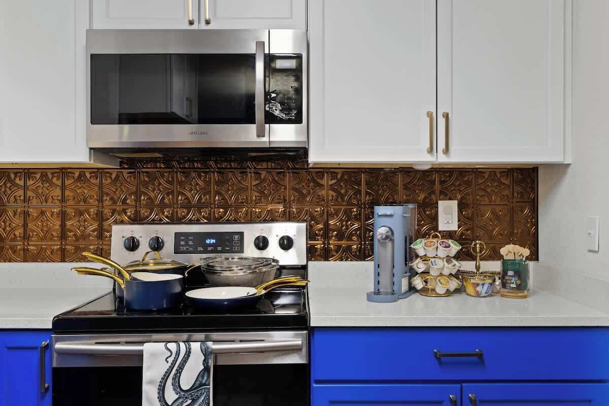 A kitchen with white cabinets, a stainless steel microwave, a stove with pots, and a decorative backsplash.