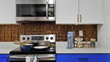 A kitchen with white cabinets, a stainless steel microwave, a stove with pots, and a decorative backsplash.