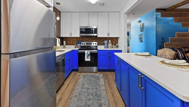 Una cocina moderna con electrodomésticos de acero inoxidable, armarios azules y piso de madera.