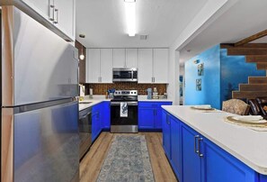 Una cocina moderna con electrodomésticos de acero inoxidable, armarios azules y piso de madera.