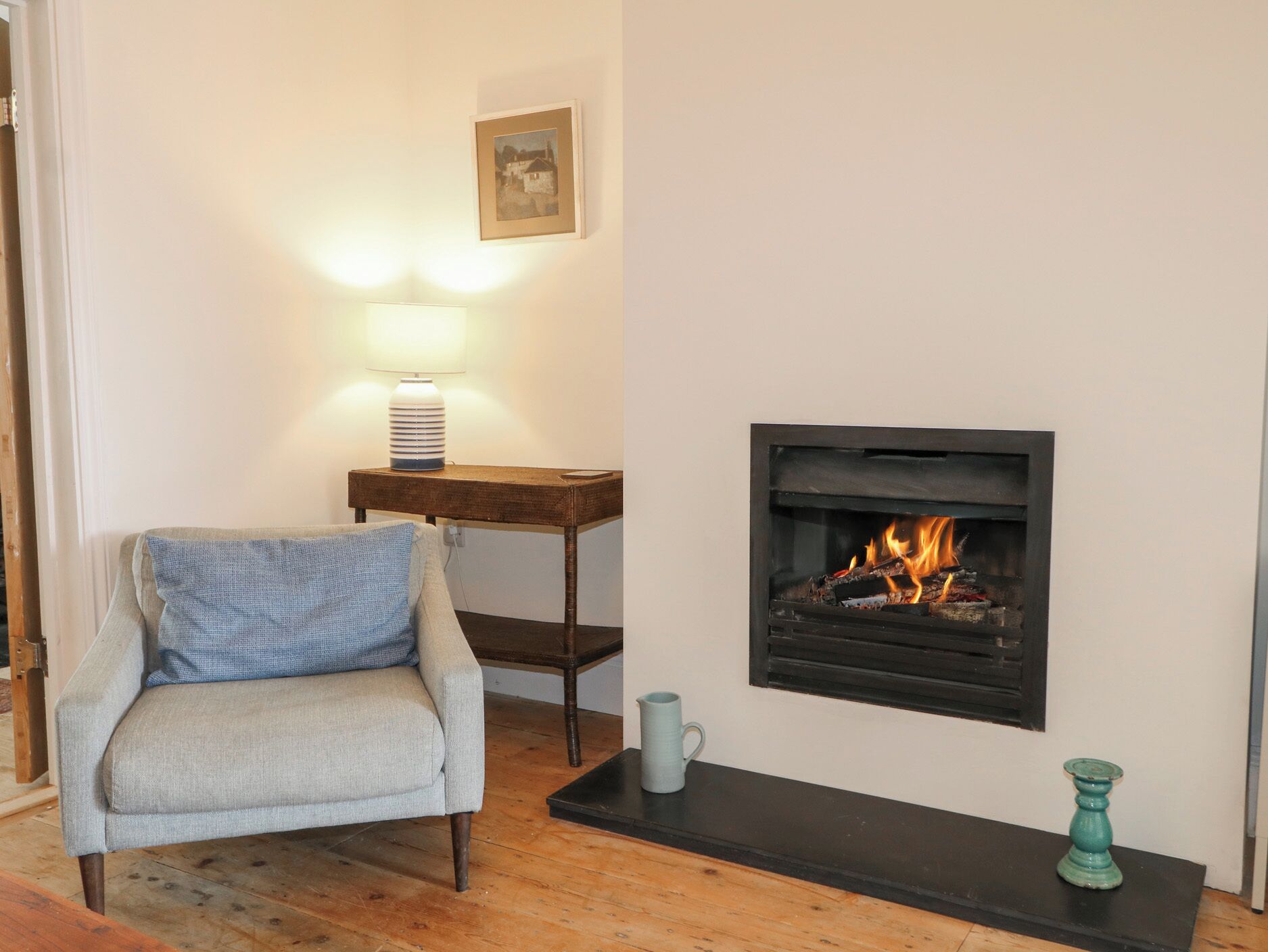 A living room with a fireplace, a sofa, a table with a lamp, and a framed picture on the wall.
