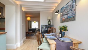 Un comedor con una mesa dispuesta para cuatro, un televisor y un cuadro con un paisaje urbano.