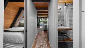 A narrow hallway with a wooden ceiling, a patterned rug, a bed, a sink, and a shower area.