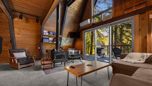 A cozy cabin interior with a fireplace, seating area, and large windows offering a view of the outdoors.