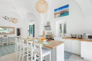A bright kitchen with white cabinetry, a wooden island, and a dining area with white chairs. - Masseria Annabella (Puglia)