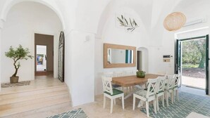 A dining area with a wooden table and white chairs, a potted plant, and a large mirror on the wall.