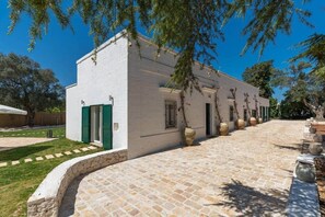 Un edificio blanco con contraventanas verdes, un camino de piedra y macetas grandes a lo largo.