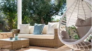 A wicker sofa with patterned cushions, a hanging chair, and a small table with a bowl and decorative items.
