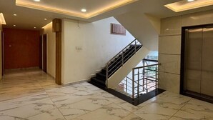 A spacious hallway with a marble floor, a staircase leading to an upper level, and recessed ceiling lighting. - Mythri Residency (Hubli)