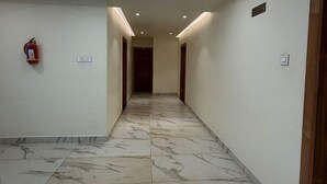 A corridor with marble flooring, recessed ceiling lighting, and a fire extinguisher on the wall. - Mythri Residency (Hubli)