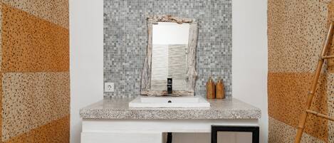 Un baño con lavamanos blanco, espejo y salpicadero de azulejos.