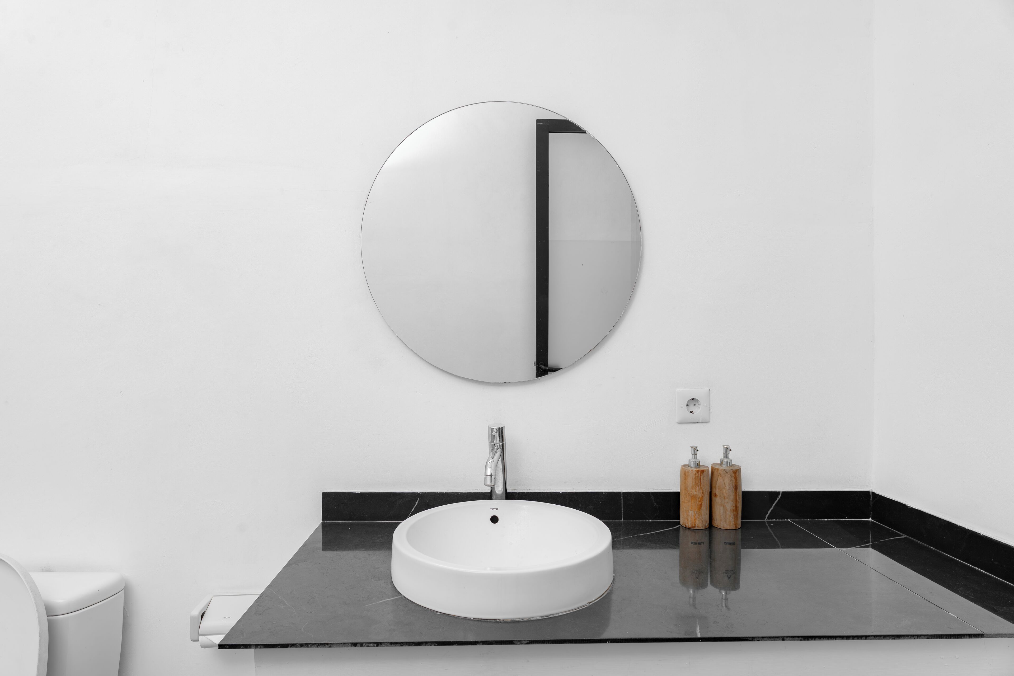 Un baño con un espejo redondo, un lavamanos blanco y dos dispensadores de jabón de madera.