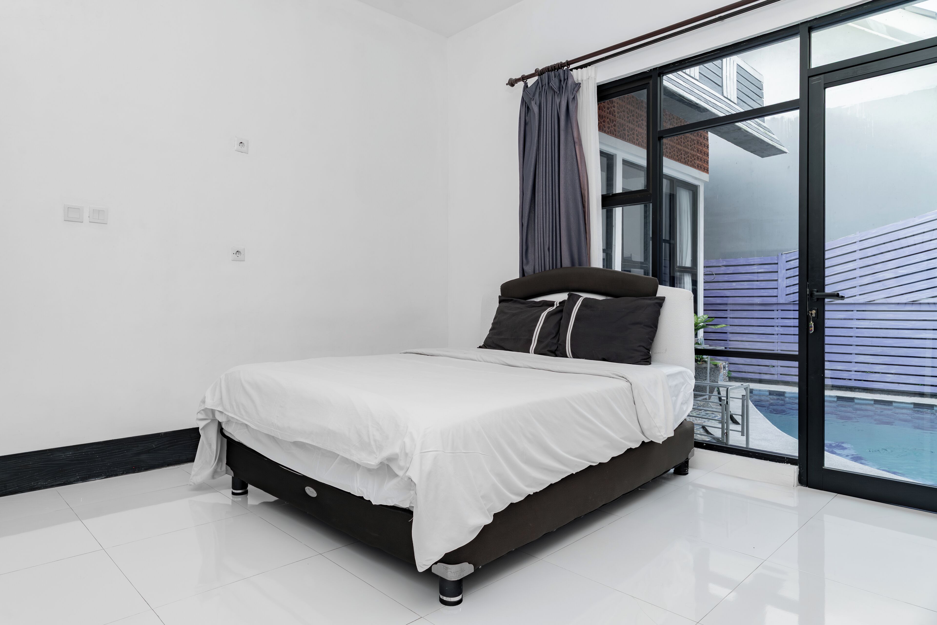 Un dormitorio moderno con una cama grande, una puerta corrediza de vidrio a un balcón y un diseño limpio y minimalista.