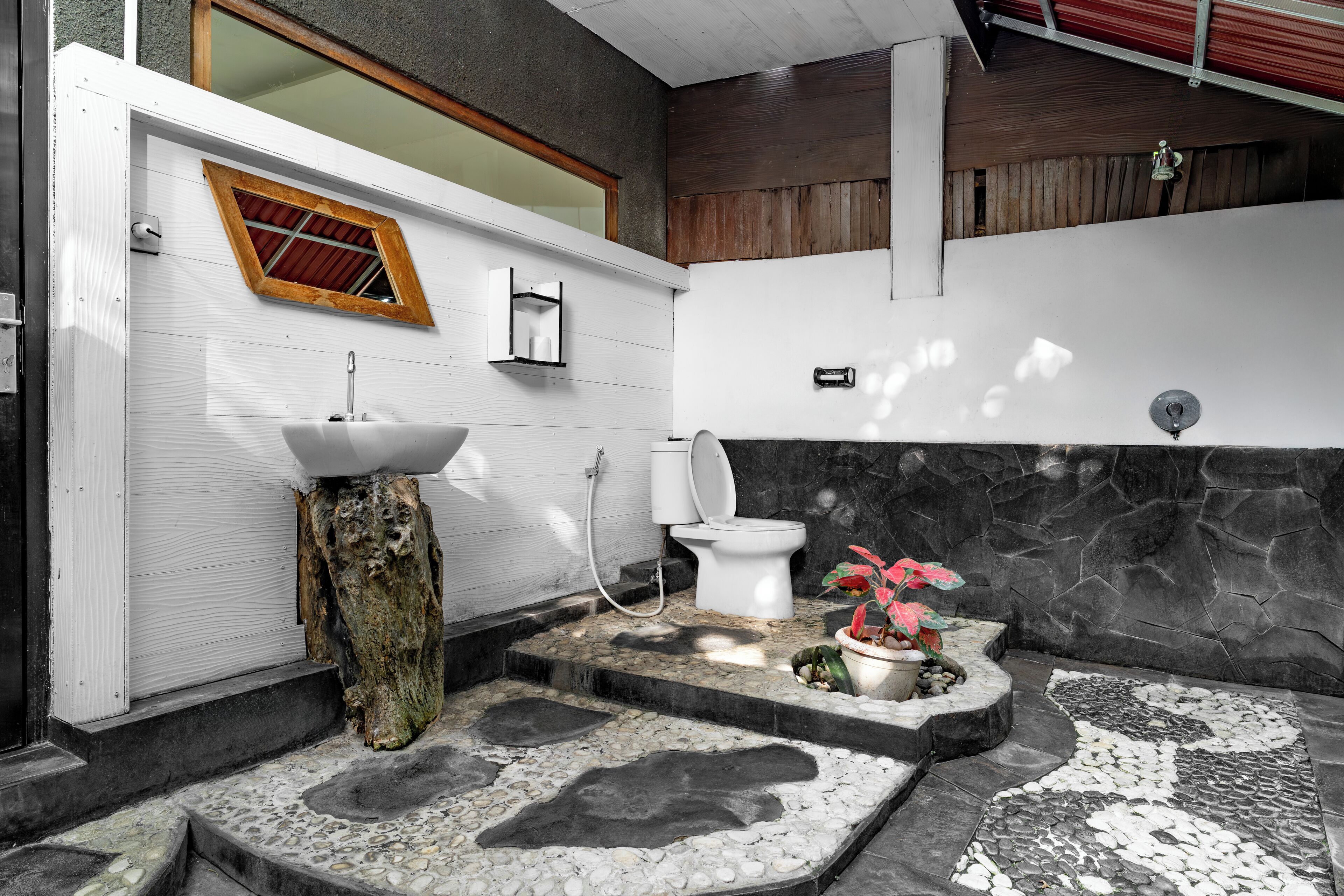 A modern bathroom with a stone sink, a toilet, and a small window.