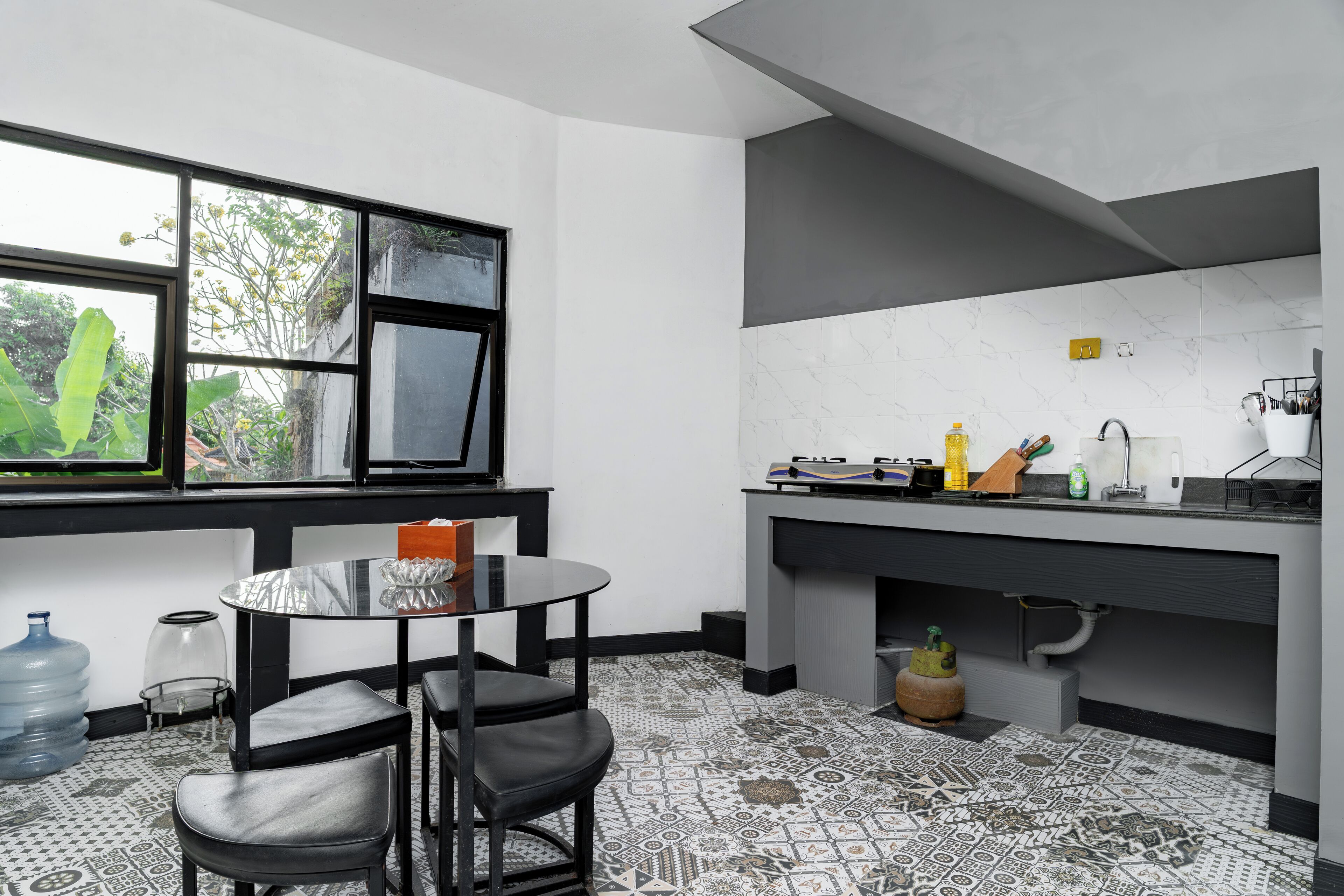 Una cocina moderna con encimera negra, ventana con vista a la vegetación y suelo estampado.