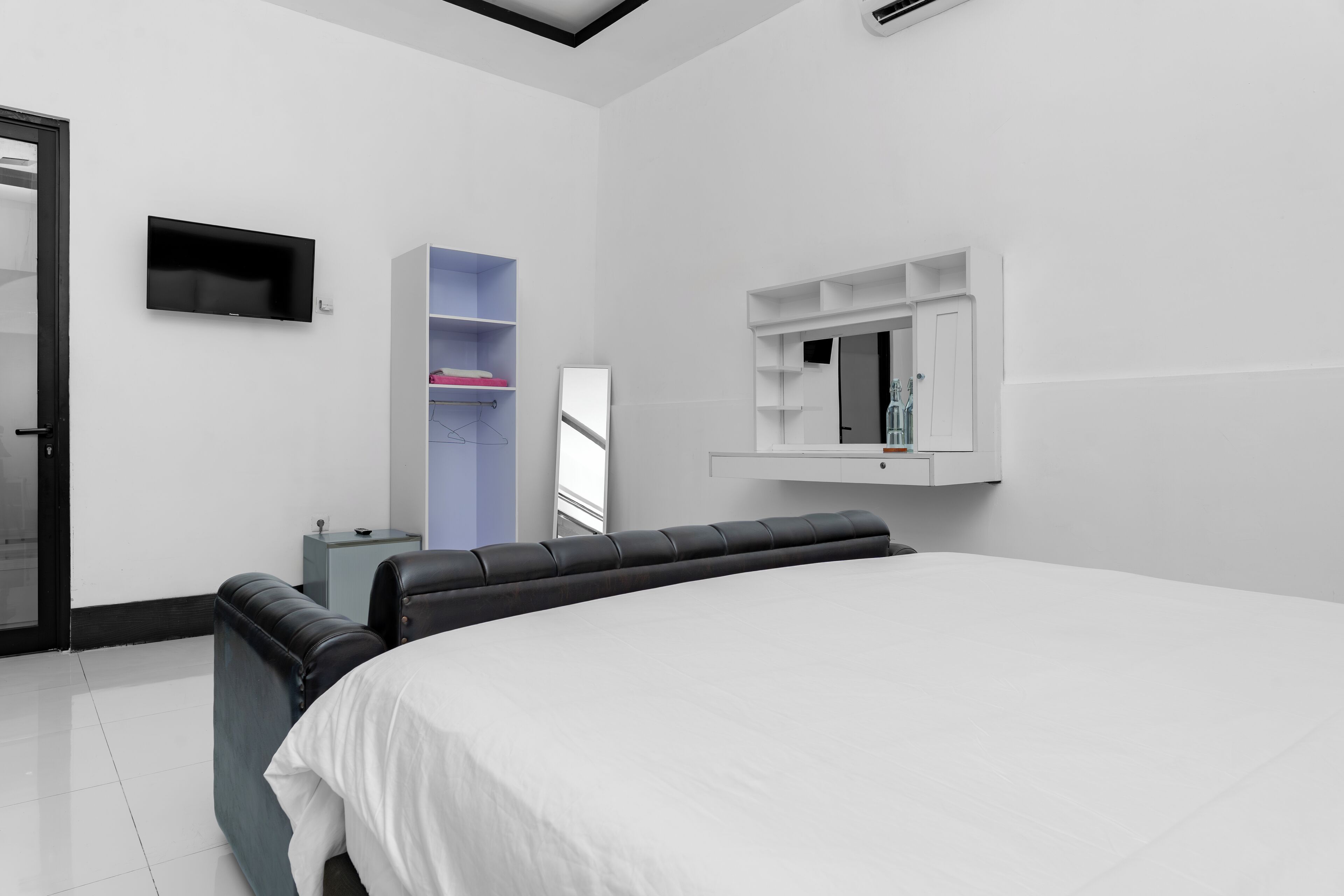 A modern hotel room with a large bed, a flat-screen TV mounted on the wall, a built-in wardrobe, and a small bedside table.