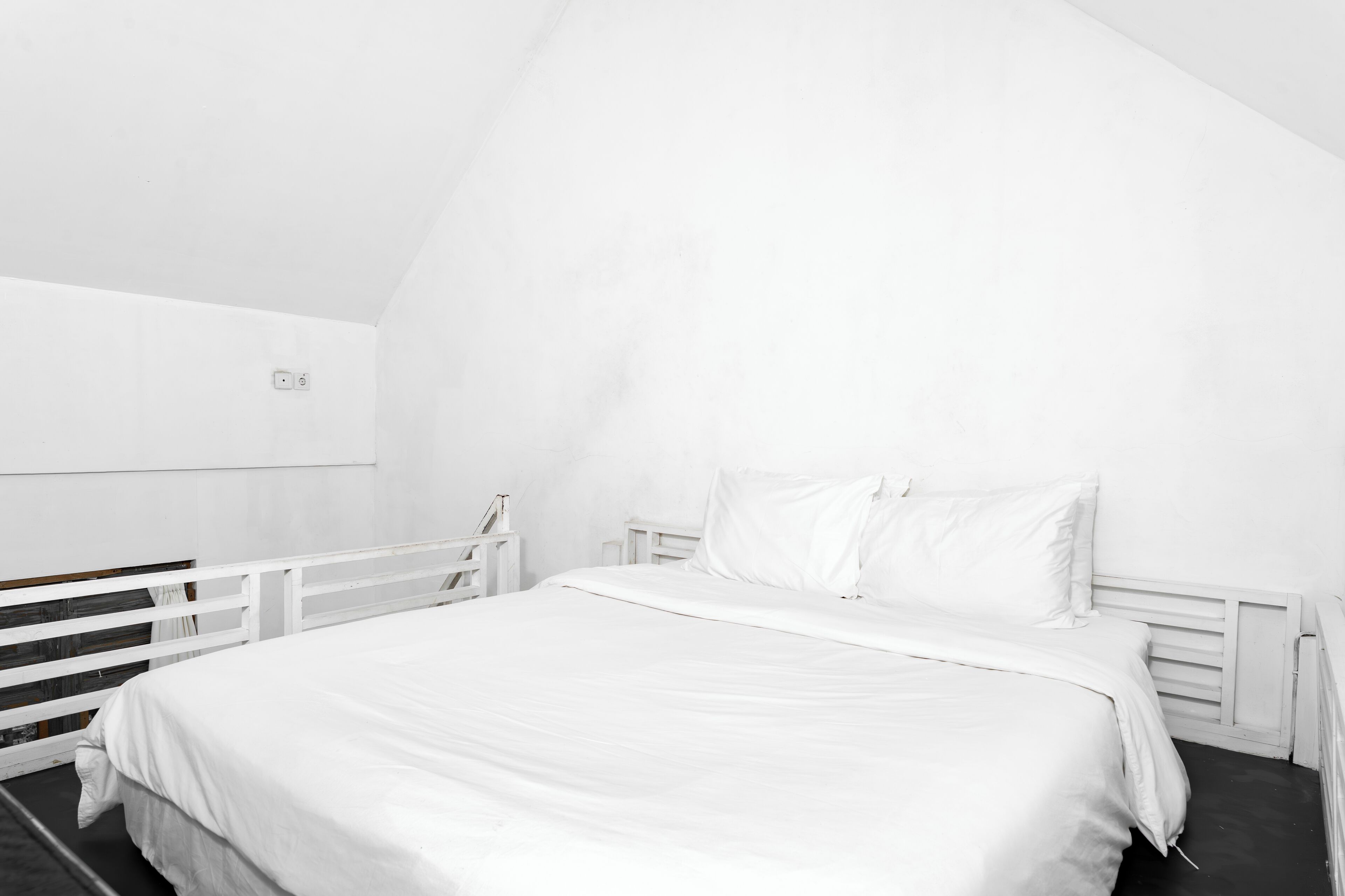 A white, modern bedroom with a sloped ceiling, a single bed with white bedding, and a white headboard.