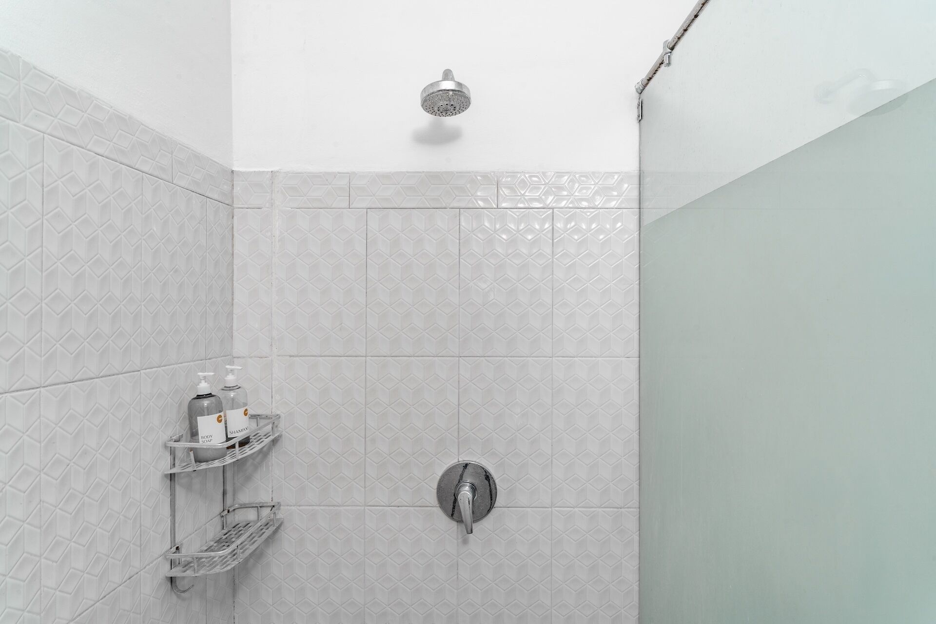 Zona de ducha con cabezal de ducha manual, grifo empotrado en la pared y estante con artículos de aseo.