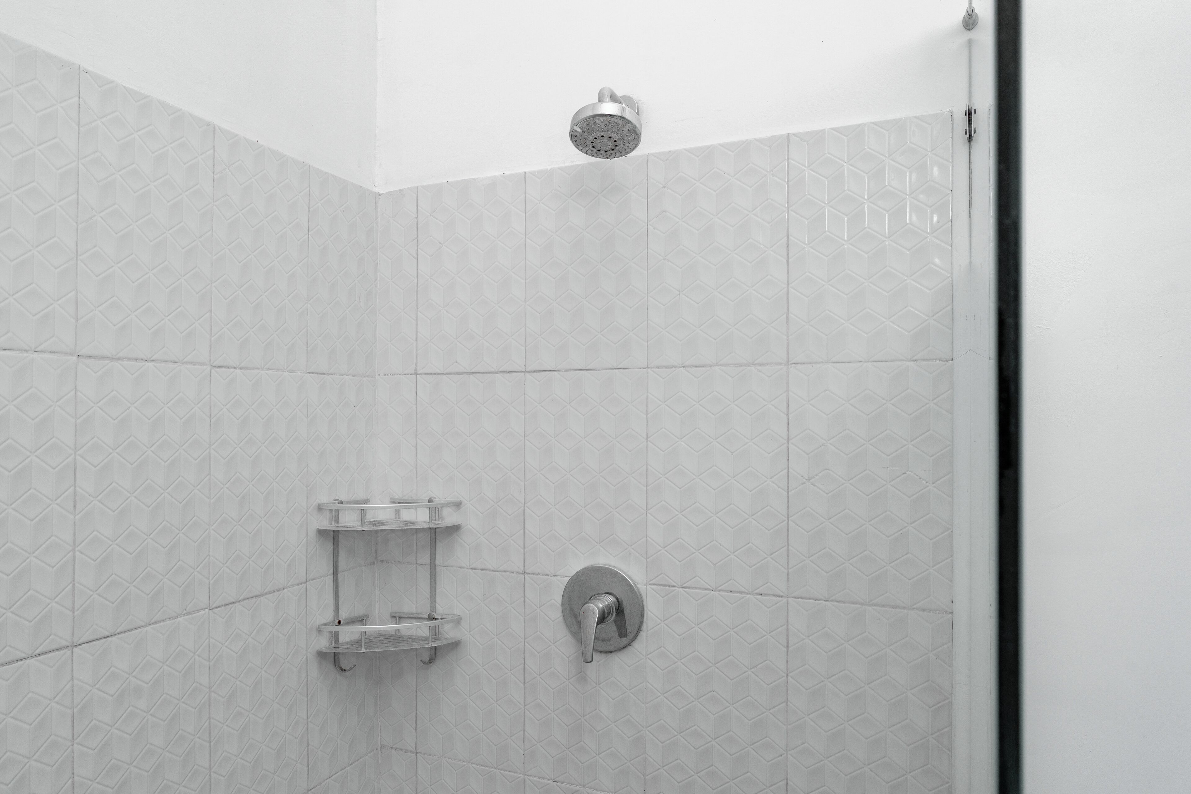 A shower area with a showerhead, a wall-mounted faucet, and a shelf with toiletries.
