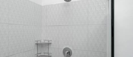 A shower area with a showerhead, a wall-mounted faucet, and a shelf with toiletries.