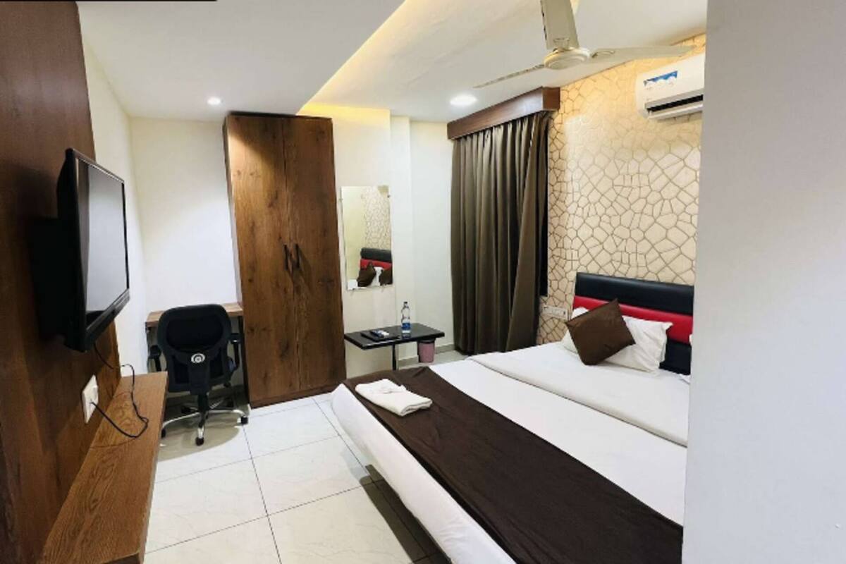 A hotel room with a bed, a desk, a chair, a television, and an air conditioning unit.