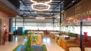 Interior de restaurante con varias áreas de estar, incluyendo mesas y sofás, bajo un techo moderno con lámparas geométricas.