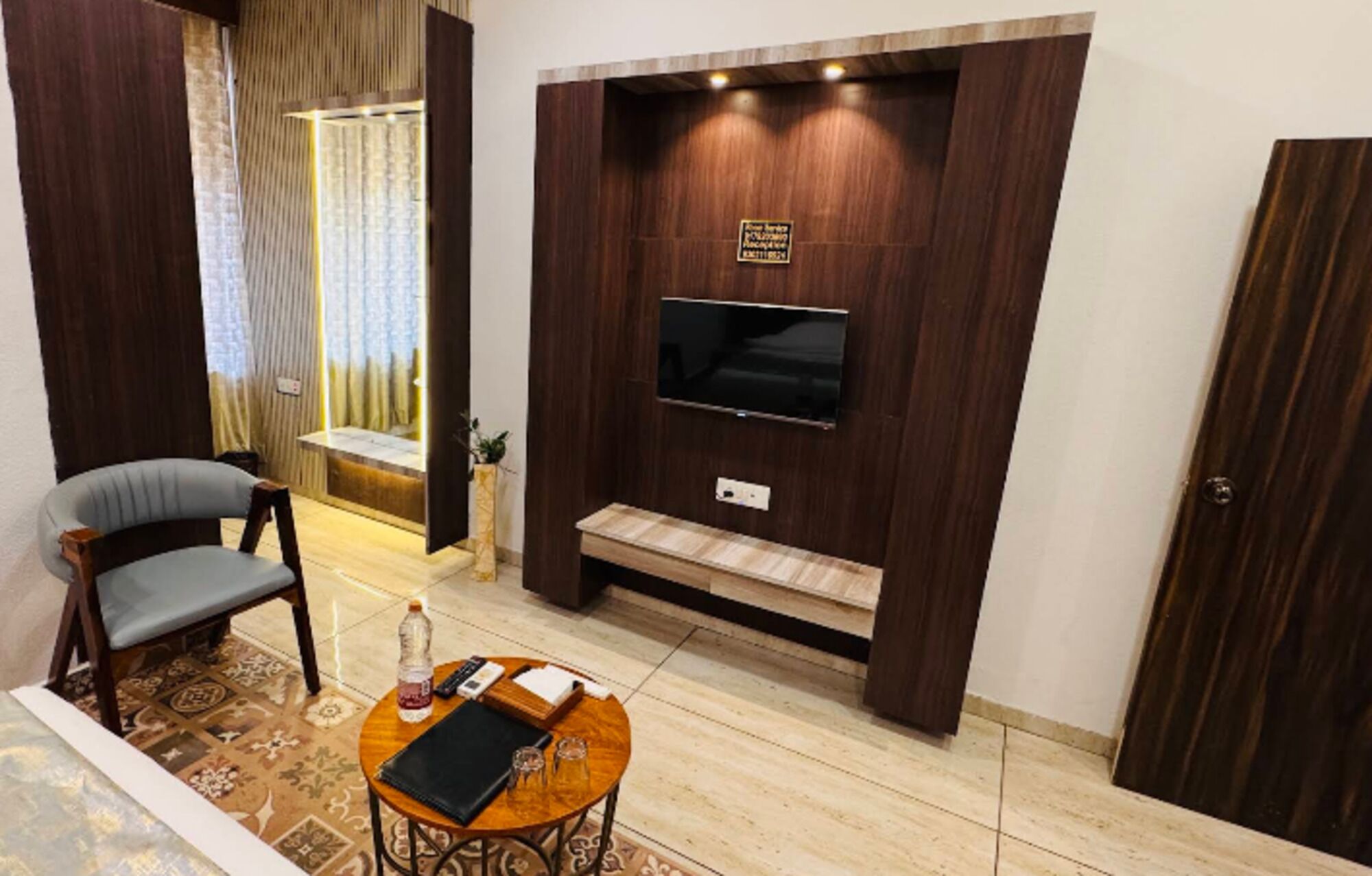 A modern living room with a flat-screen TV mounted on a wooden wall, a seating area with a chair, a small coffee table, and a decorative rug.