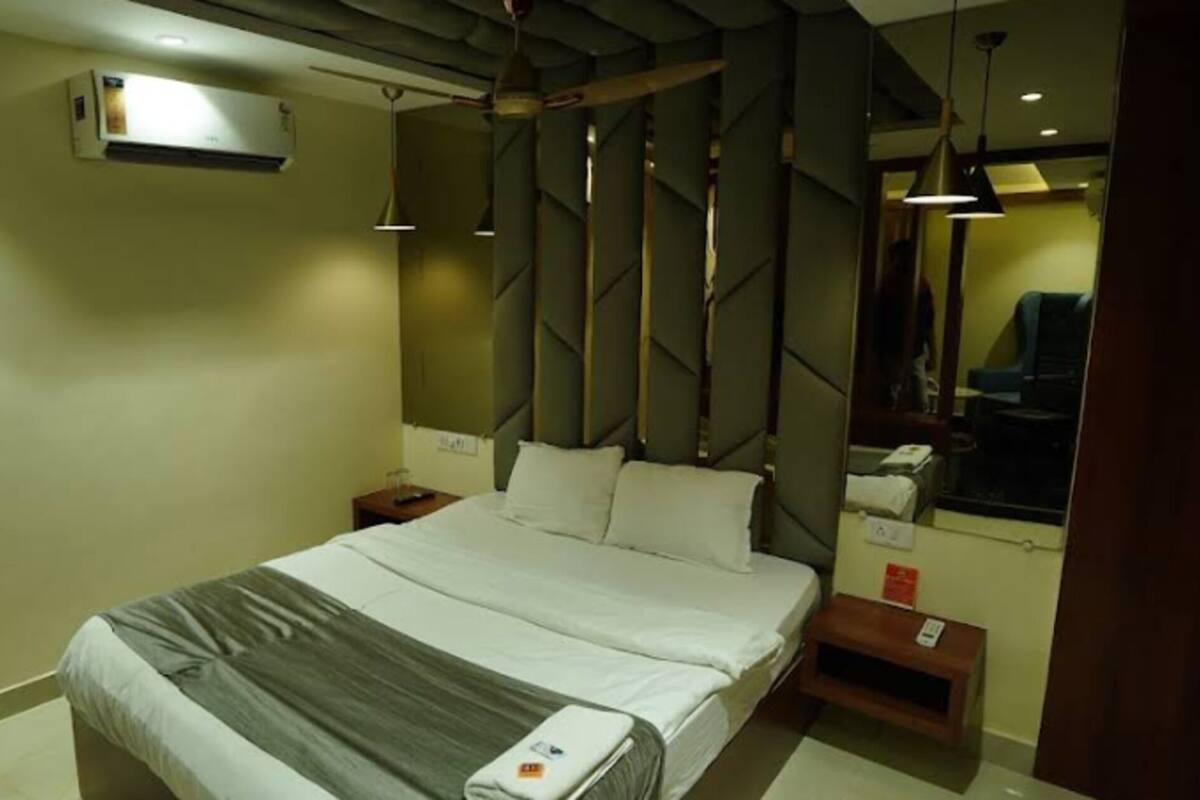 A hotel room with a bed, bedside tables, an air conditioning unit, and a mirror.