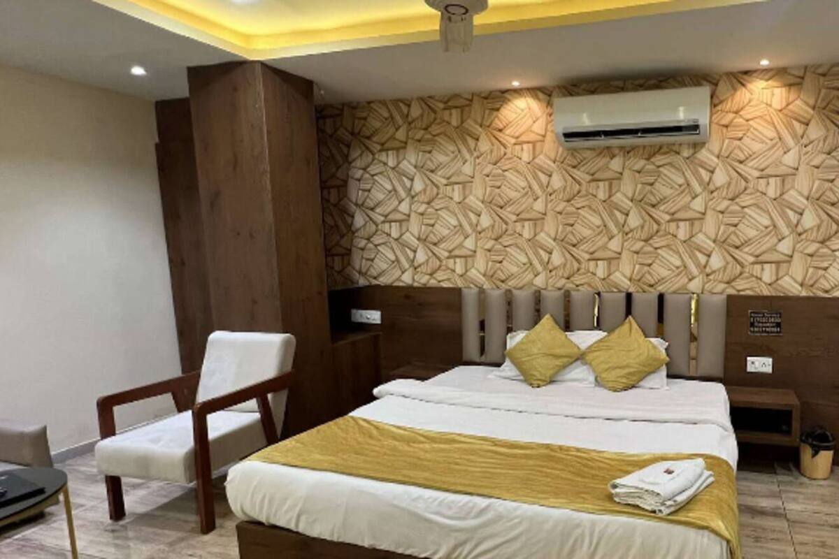 A hotel room with a bed, a chair, an air conditioning unit, and a wooden wall design.