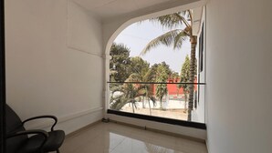 Una habitación con un amplio ventanal de arco, una silla negra y suelo de baldosas.